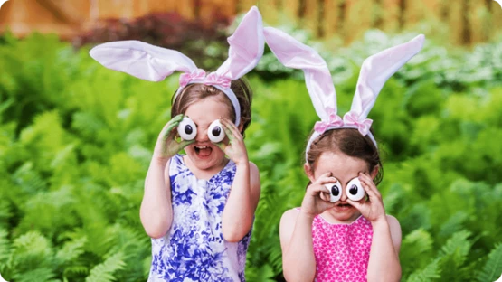 Two girls with animal ear hairbands holding up homemade animal eyes infront of their faces