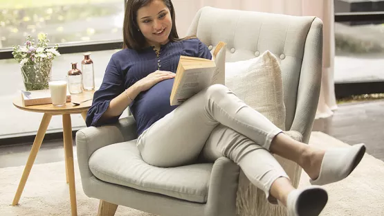 Pregnant woman sitting on sofa reading a book